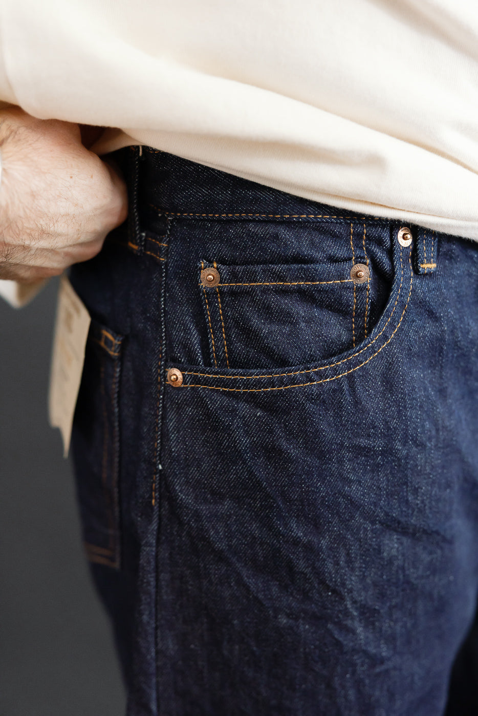 Close-up of the front right hip of dark indigo selvedge denim jeans on a male model.