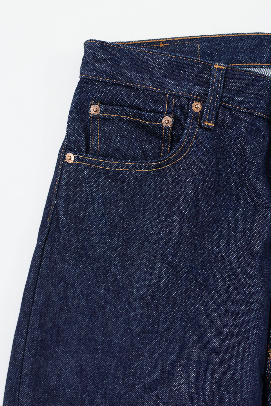 Close-up of the front waist and pocket area of dark indigo selvedge denim jeans.