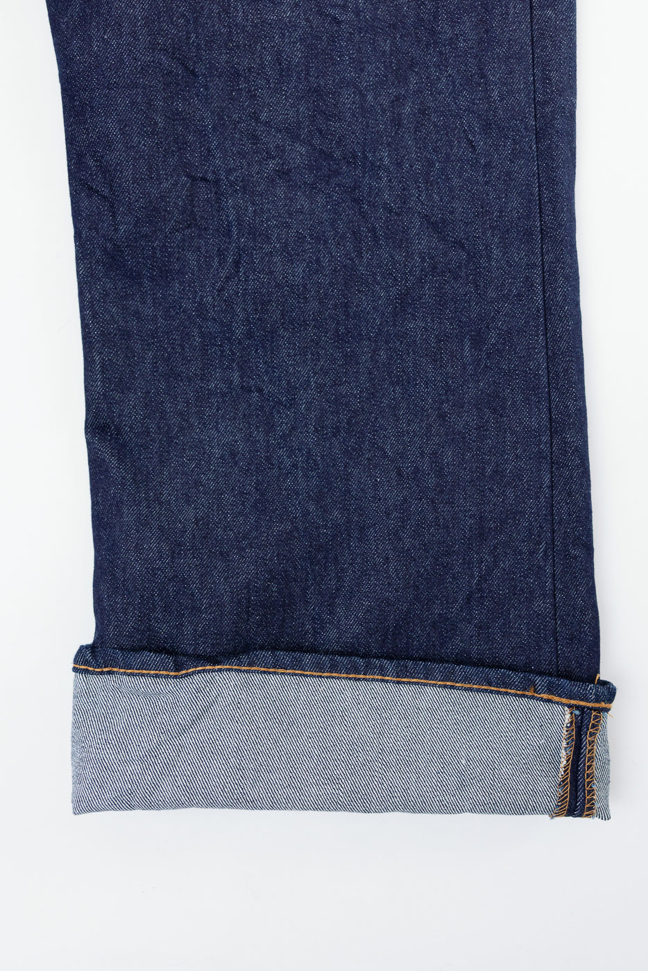 Close-up of the cuffed hem and selvedge detail on the bottom of dark indigo denim jeans.