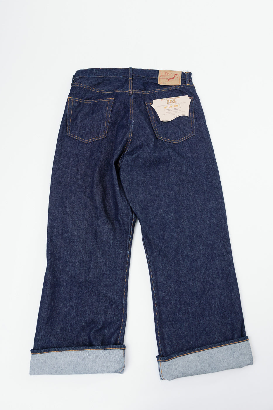 Back view flat lay of dark blue selvedge denim jeans with cuffed hems and a tan leather patch.