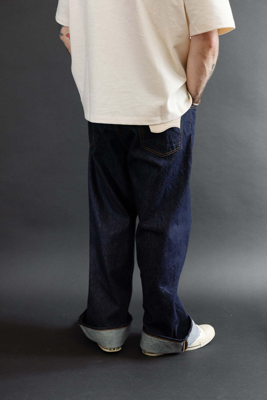 Back view full body of male model wearing dark indigo selvedge denim jeans and a cream t-shirt.