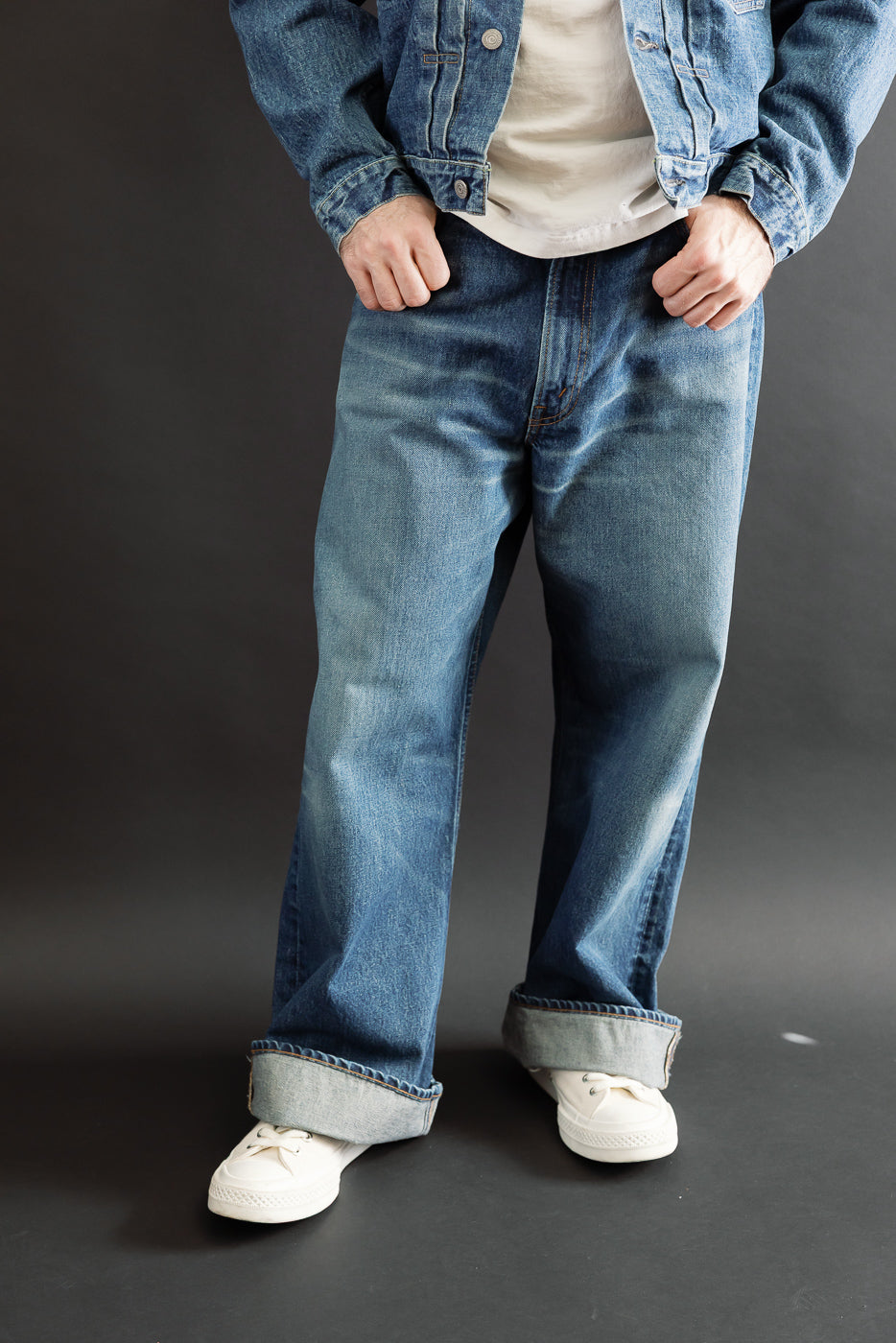 Full body front view of a male model with an athletic build wearing blue denim jeans and a jacket.