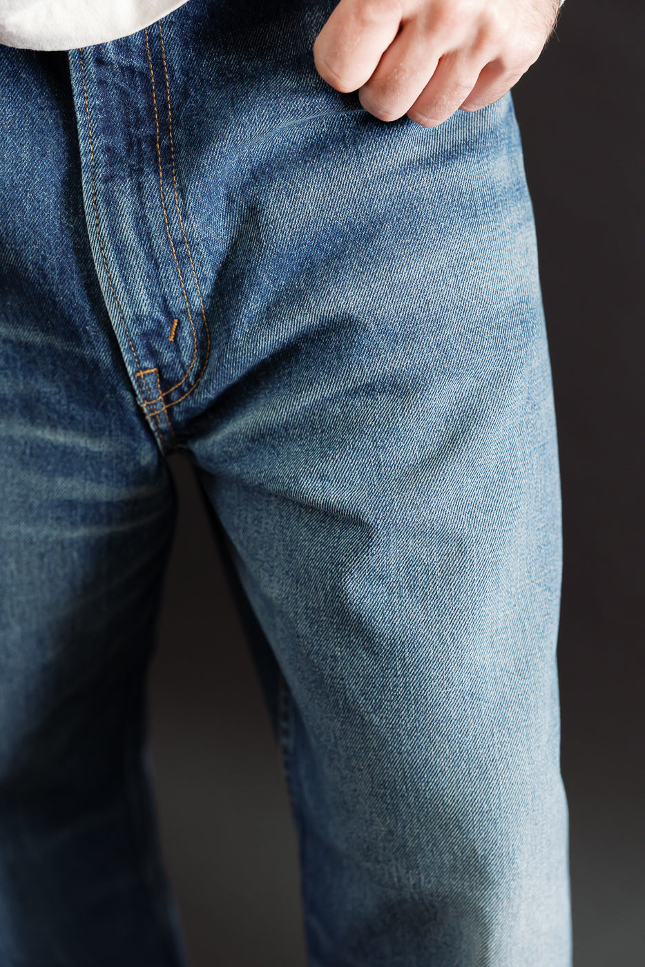 Close-up of the front left hip and denim fabric texture on blue jeans worn by an athletic male model.