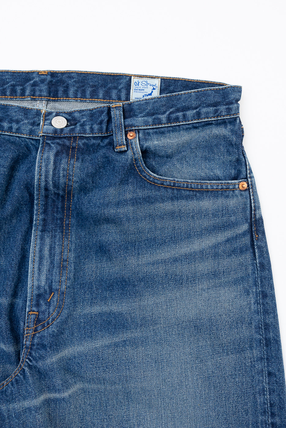 Front view flat lay close-up of blue denim jeans showing waistband, button, and pocket detail.
