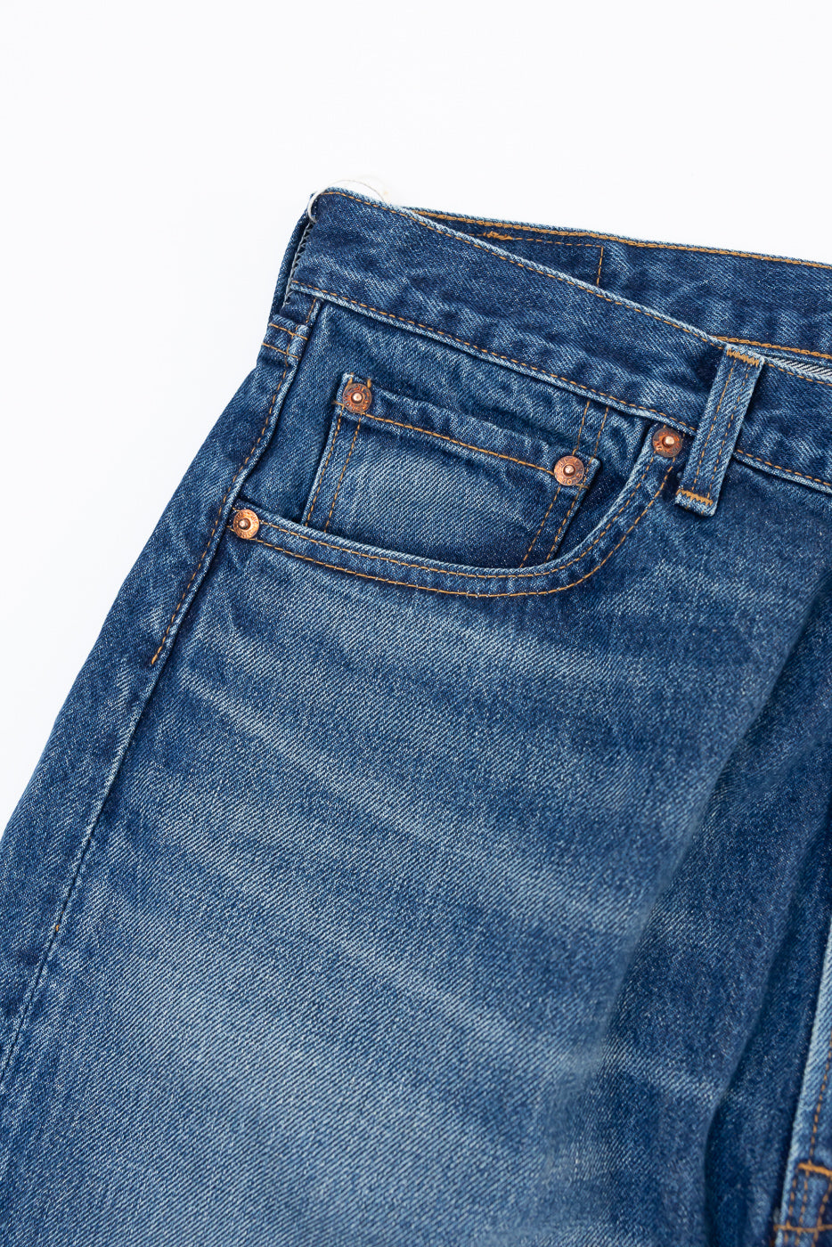 Close-up of the front waist and coin pocket of blue denim jeans showing fabric texture.