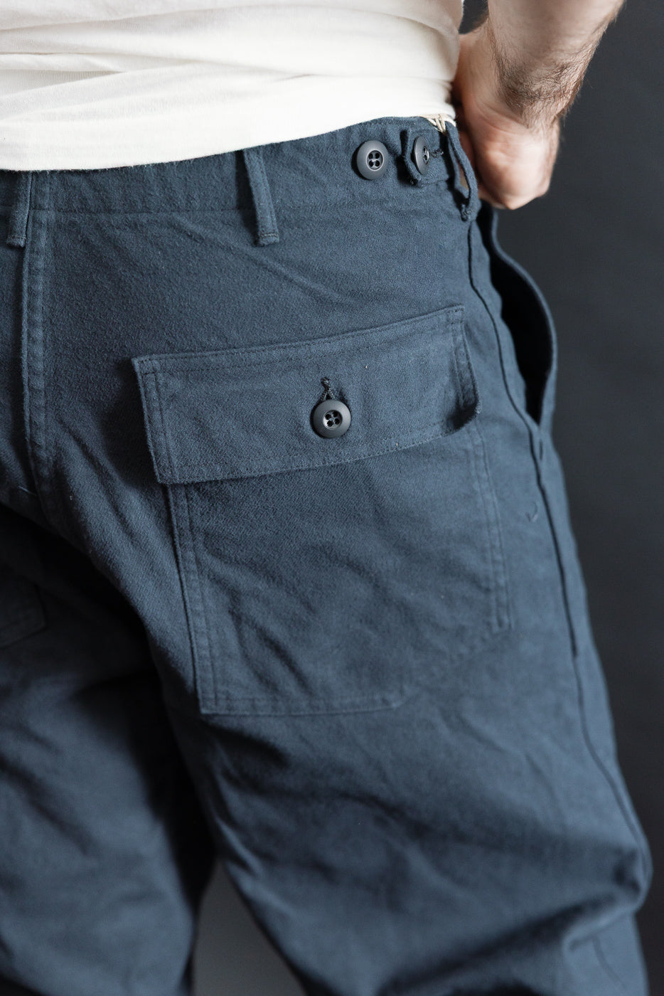 Close-up of back right side of Orslow fatigue pants in dark navy brushed flannel on male model, showing button flap pocket and waistband detail. Model is 5'9