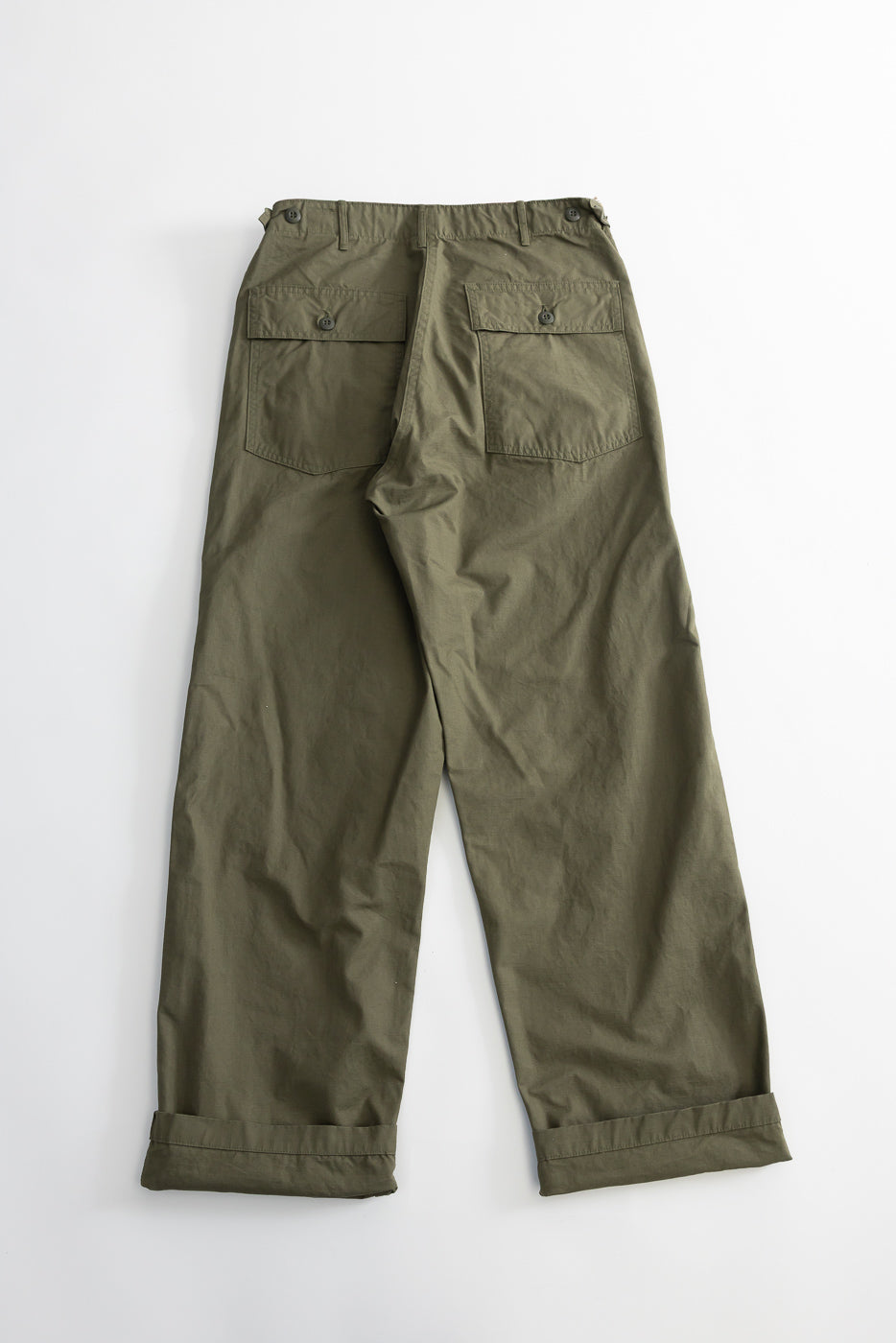 Flat lay of army green fatigue pants, back view showing buttoned flap pockets and cuffed hems.