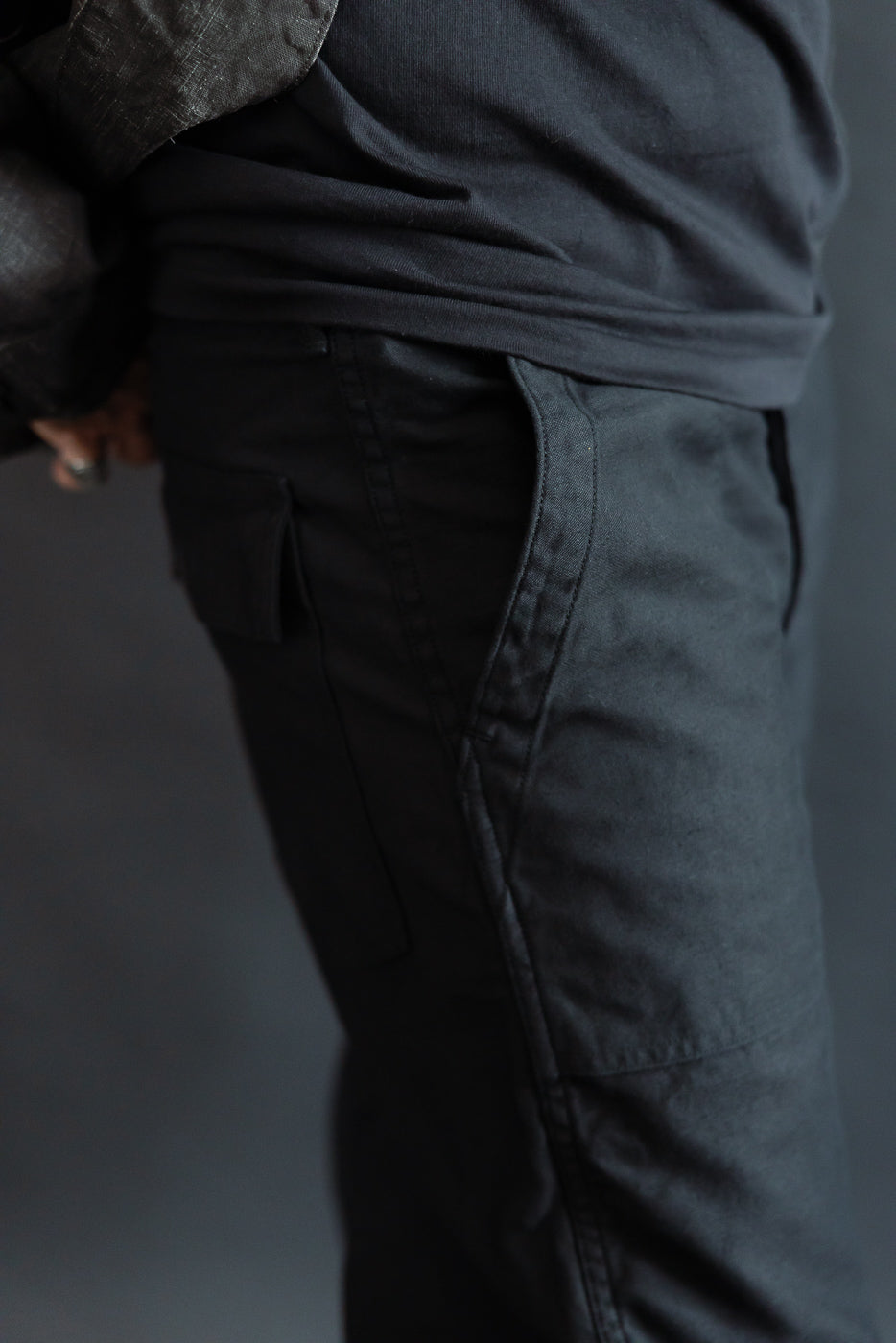 Close-up right side view of deep black fatigue pants on male model, detail of pocket and fabric texture, model is 5'9