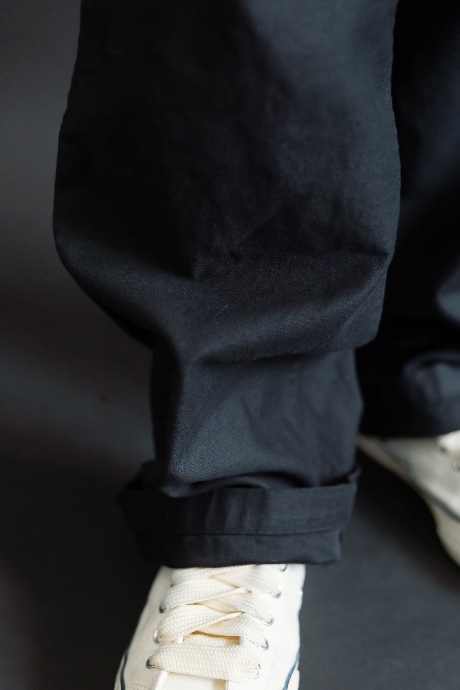 Close-up of male model’s lower front pant leg and cuff on deep black fatigue pants, showing reverse sateen texture, paired with white sneakers. Model is 5'9