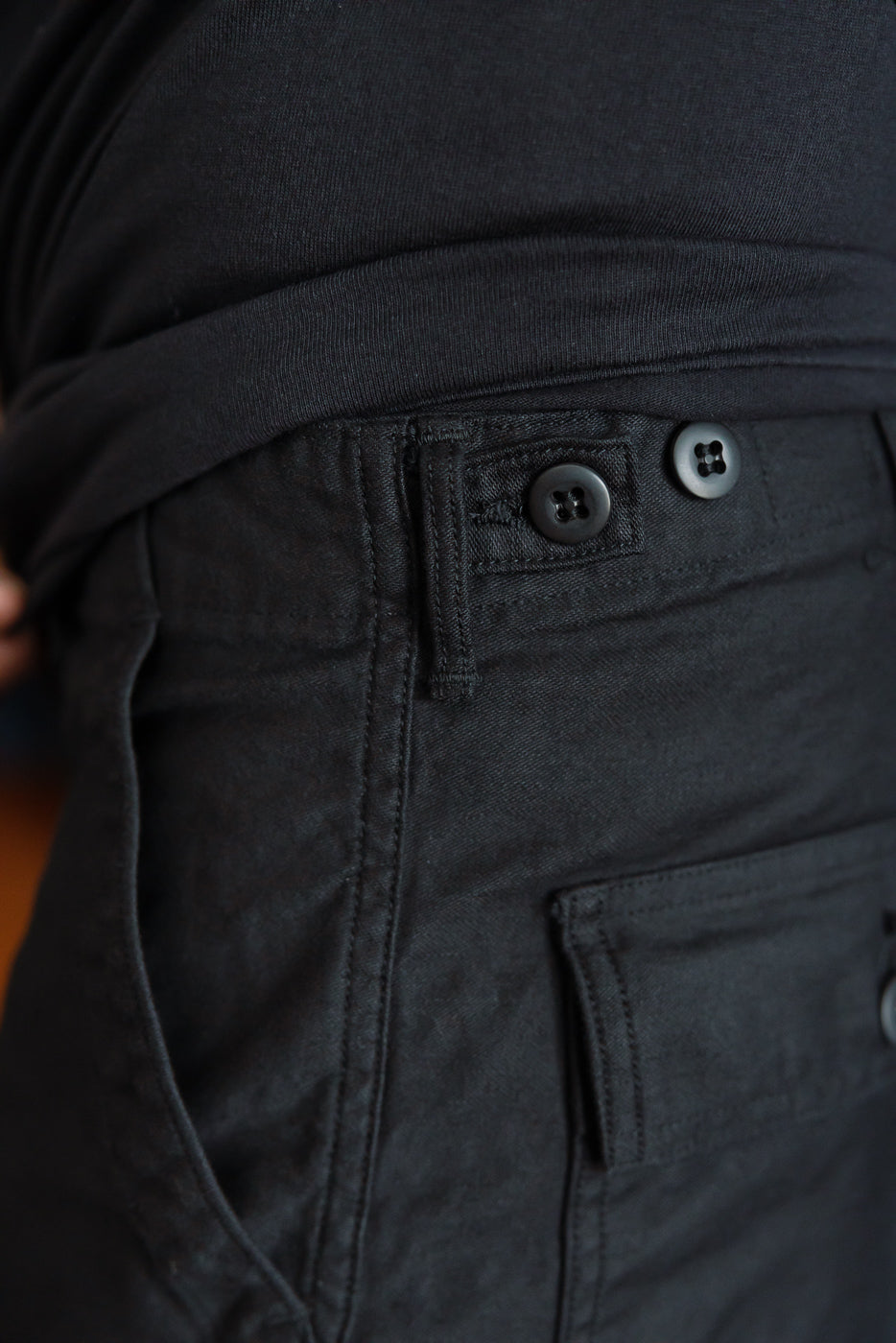 Close-up of front waist and pocket on deep black reverse sateen fatigue pants, male model, side view