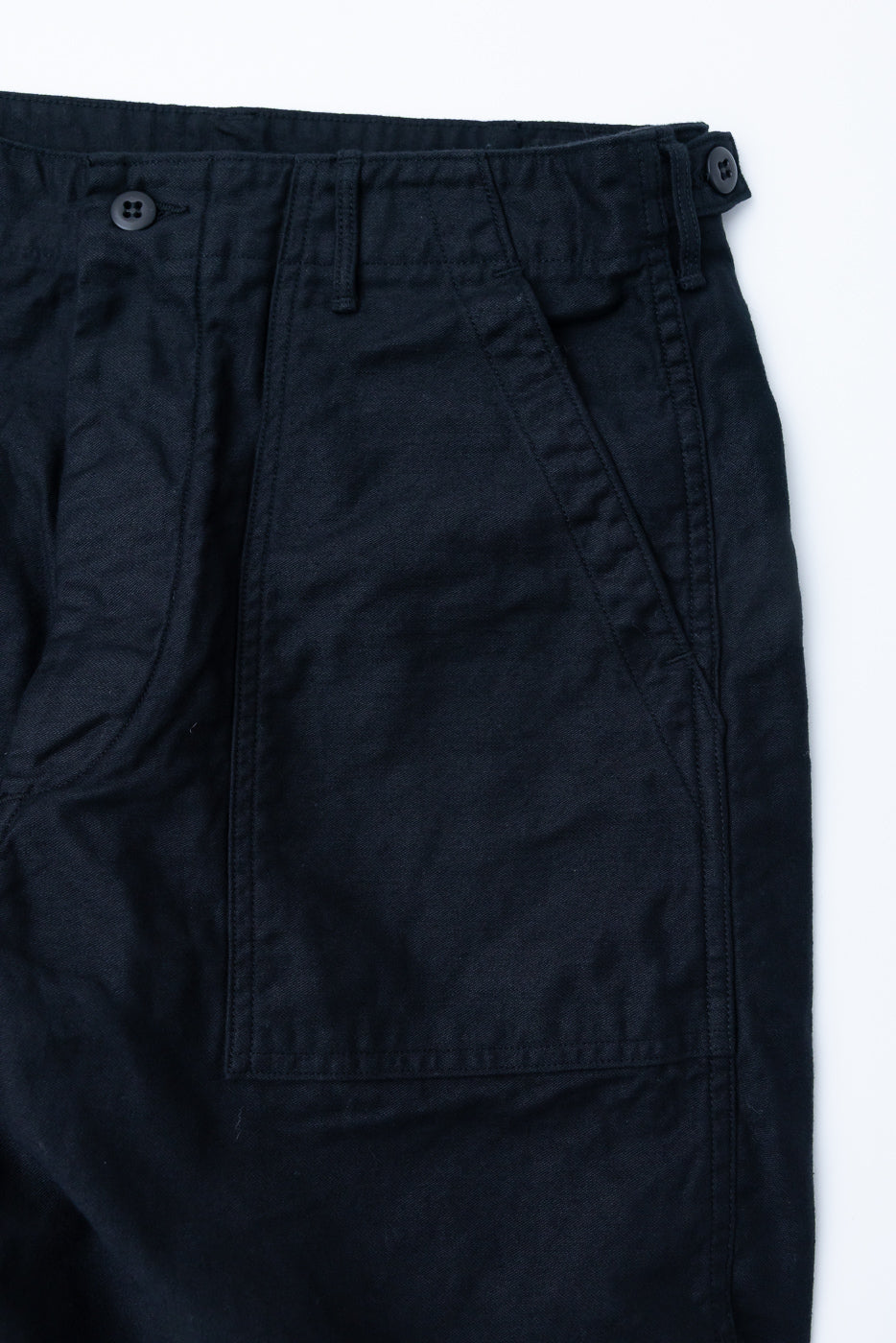 Close-up of front left side of deep black fatigue pants, showing button waist, belt loop, waist adjuster, and slant pocket detail.