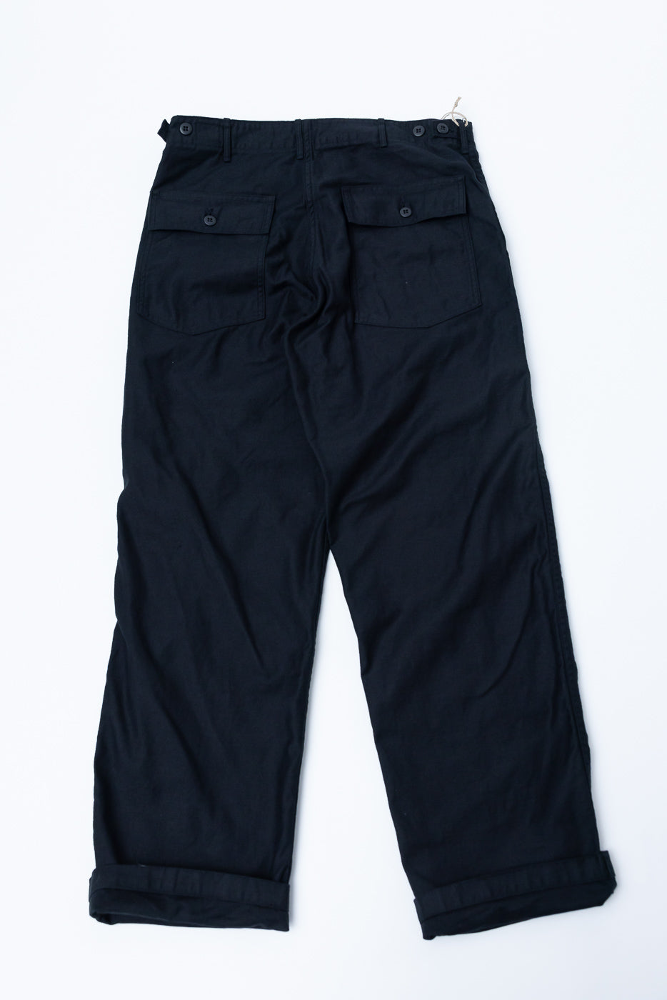Flat lay of fatigue pants in deep black, back view showing buttoned rear pockets and cuffed hems.