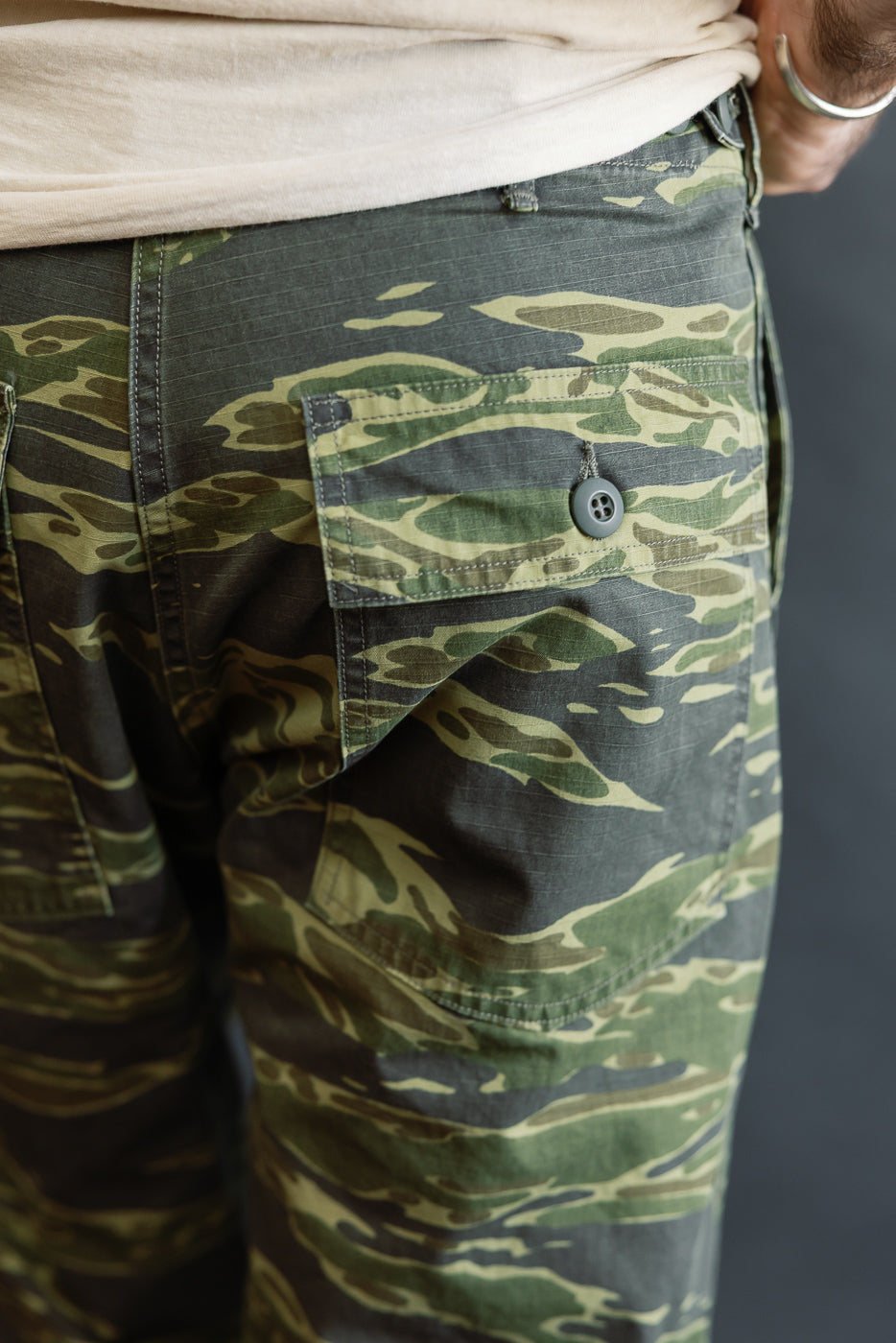 Close-up of orSlow 01-5002-TGC Fatigue Pants Ripstop Standard Fit in Tiger Camo, highlighting a side flap pocket with button and visible light-colored shirt hem above waistband.