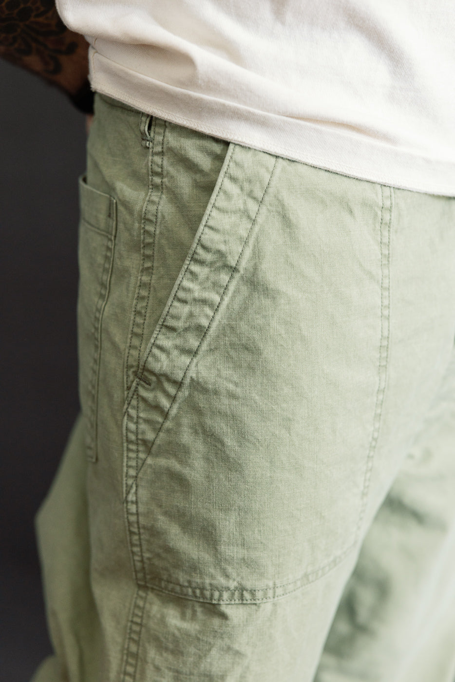 Close-up side view of male model's olive green cargo pants, showing front pocket & stitching detail