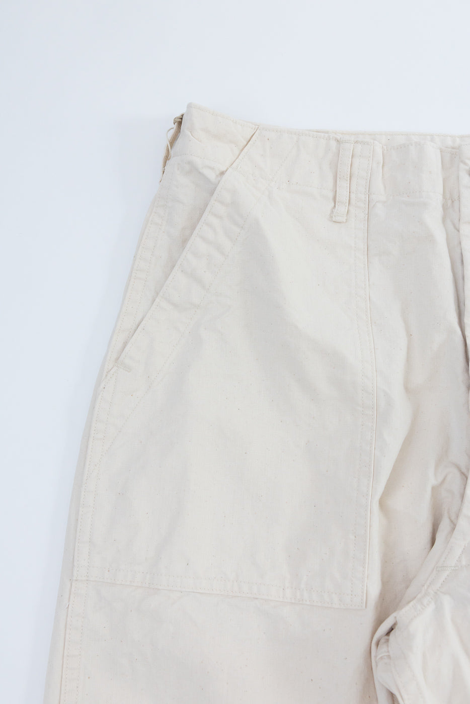 Close-up front view of beige cargo pants showing pocket stitching, waistband, and fabric texture