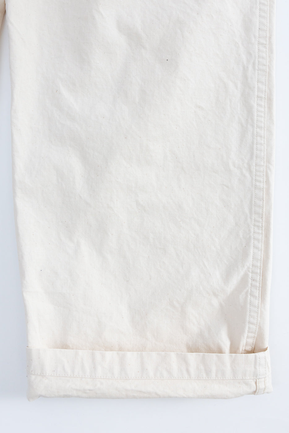 Close-up front view of off-white casual pants, showing cuffed hem and fabric texture