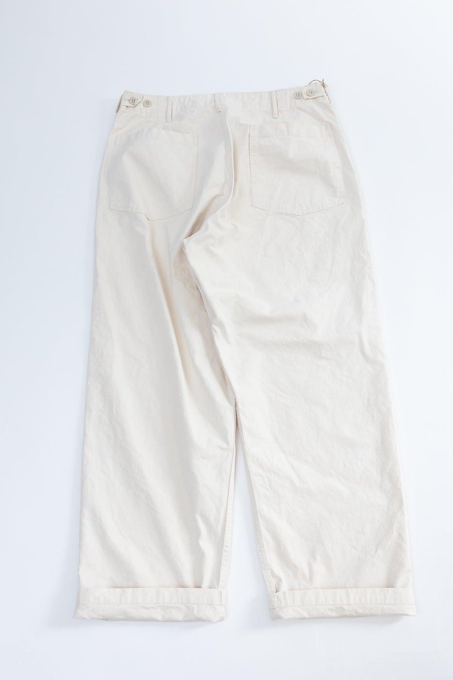 Back view flat lay of off-white wide-leg pants with cuffed hems, button closures, and rear pockets