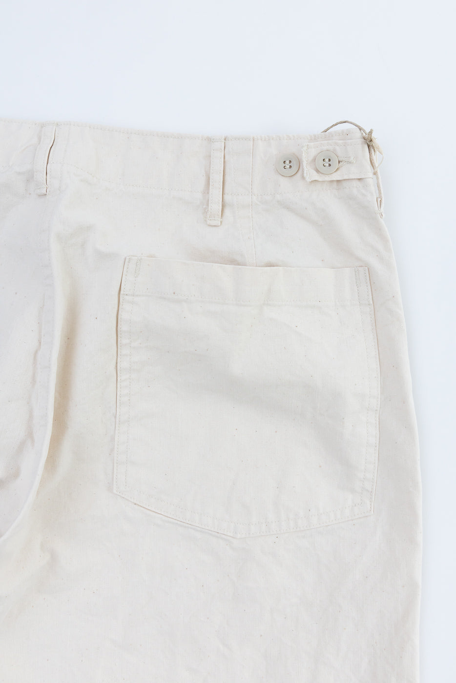 Flat lay close-up of off-white casual pants front, showing button fly, belt loops, and front pocket detail