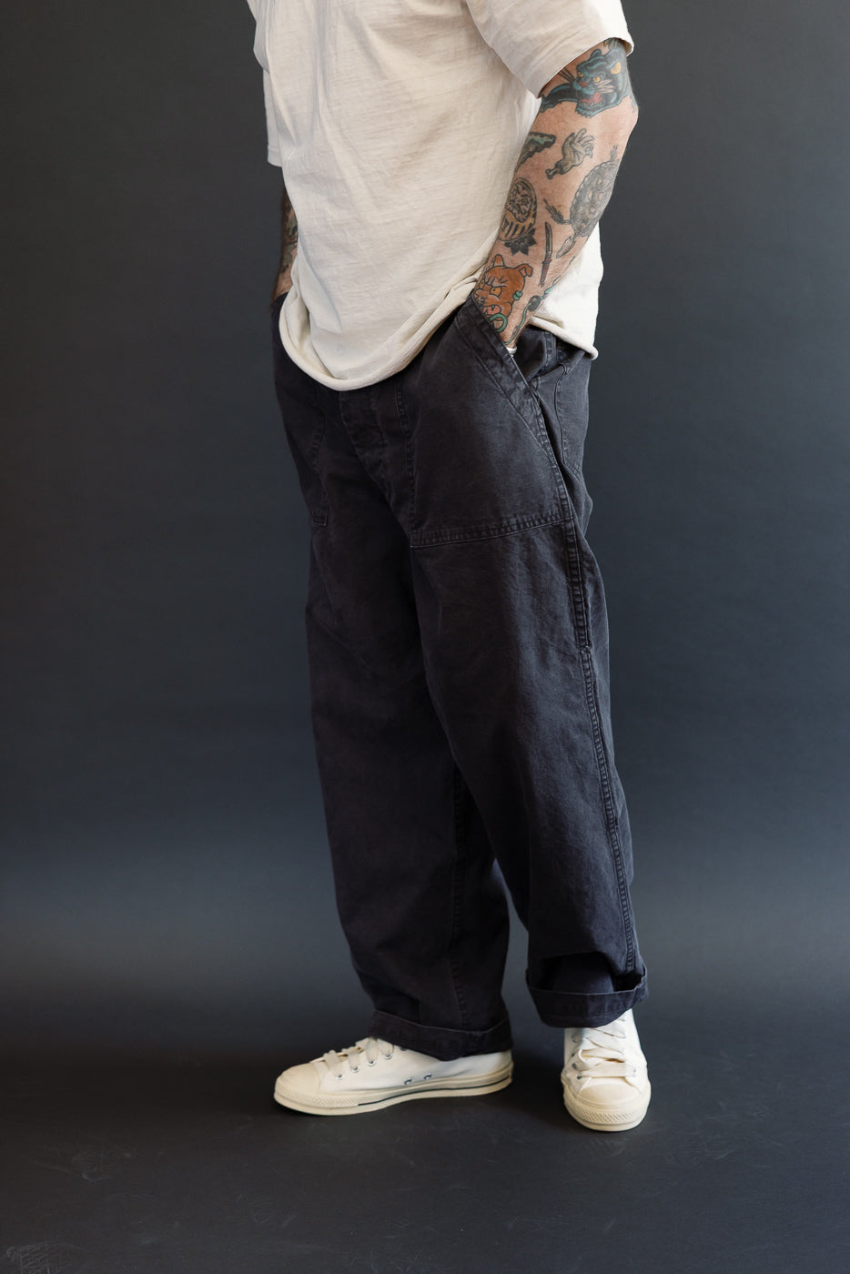 A casually dressed person showcases the orSlow 01-5103-M61K - Duck Canvas Summer Fatigue Pants - Black, featuring a wide, roomy fit with hands tucked into deep pockets, highlighting the pants' relaxed style.