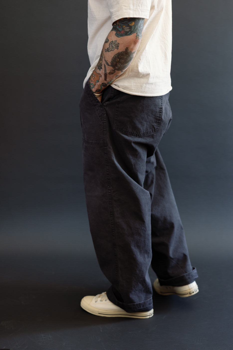 A person in profile wears orSlow 01-5103-M61K Duck Canvas Summer Fatigue Pants in black, showcasing a high-rise wide fit with hands in deep pockets, highlighting casual comfort and style.