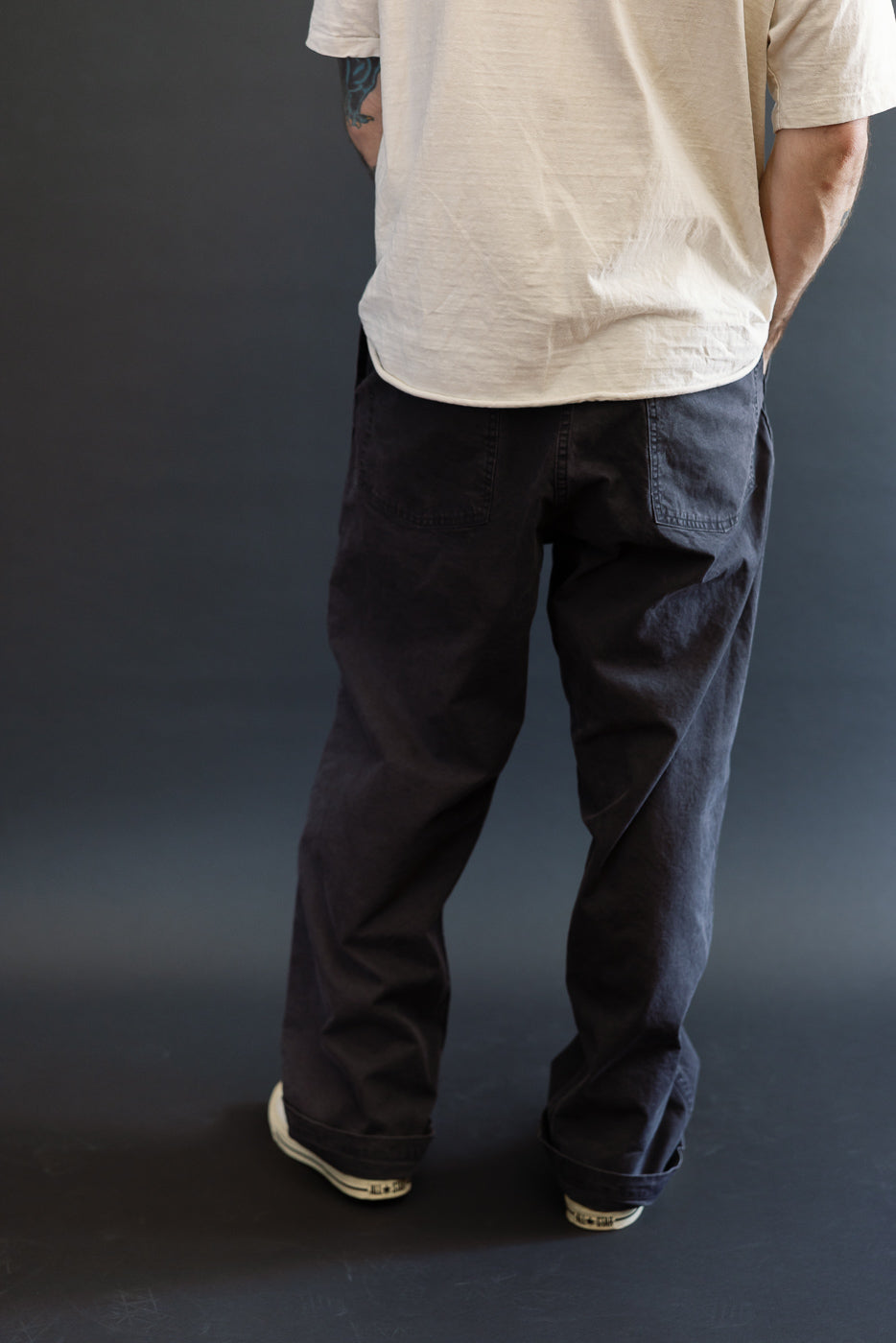 Person wearing the orSlow 01-5103-M61K Duck Canvas Summer Fatigue Pants in black, showcasing a high rise, wide leg fit, and visible rear patch pockets, styled with white sneakers.