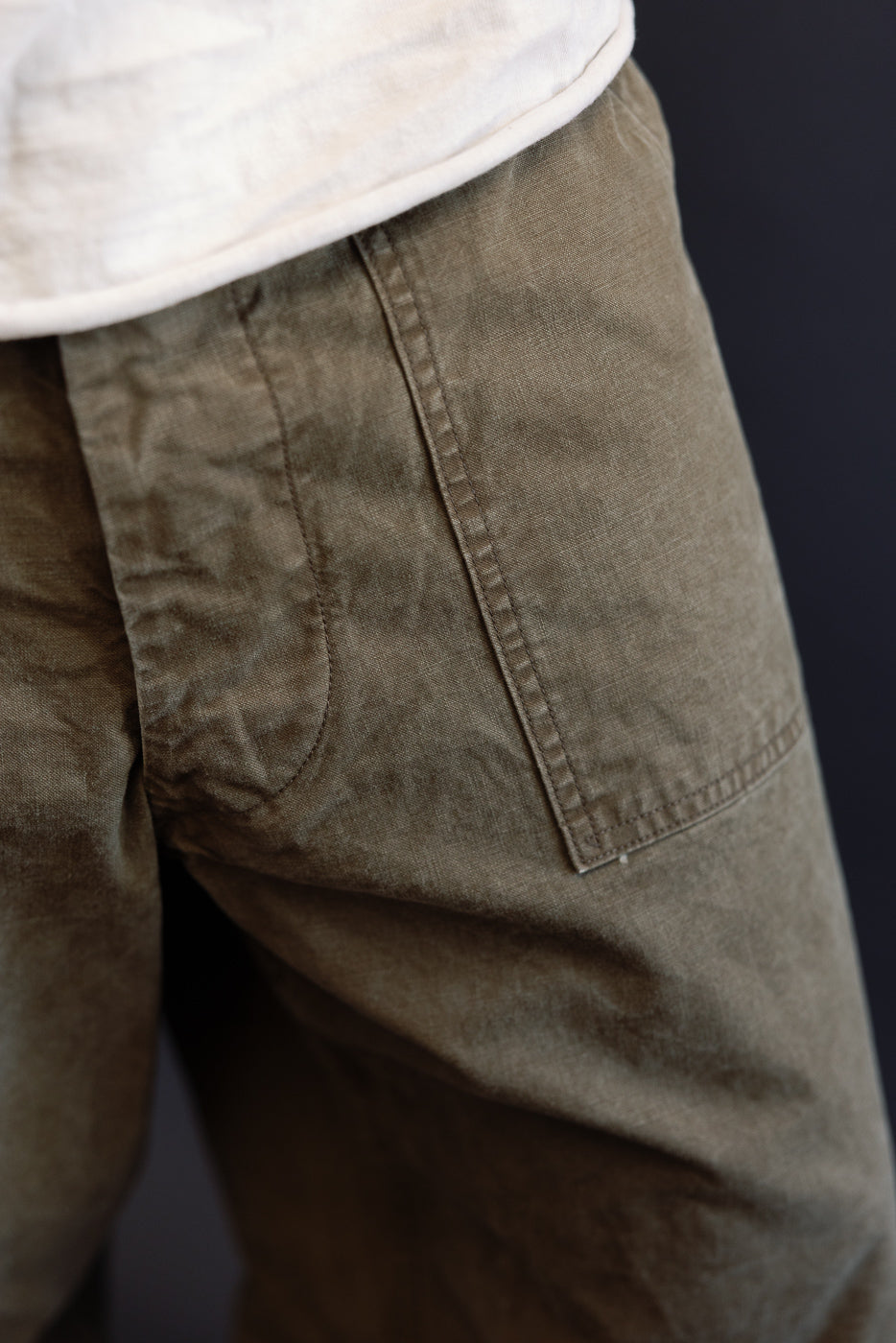 Close-up front view of olive cargo pants on male model, showing side pocket stitching and fabric texture
