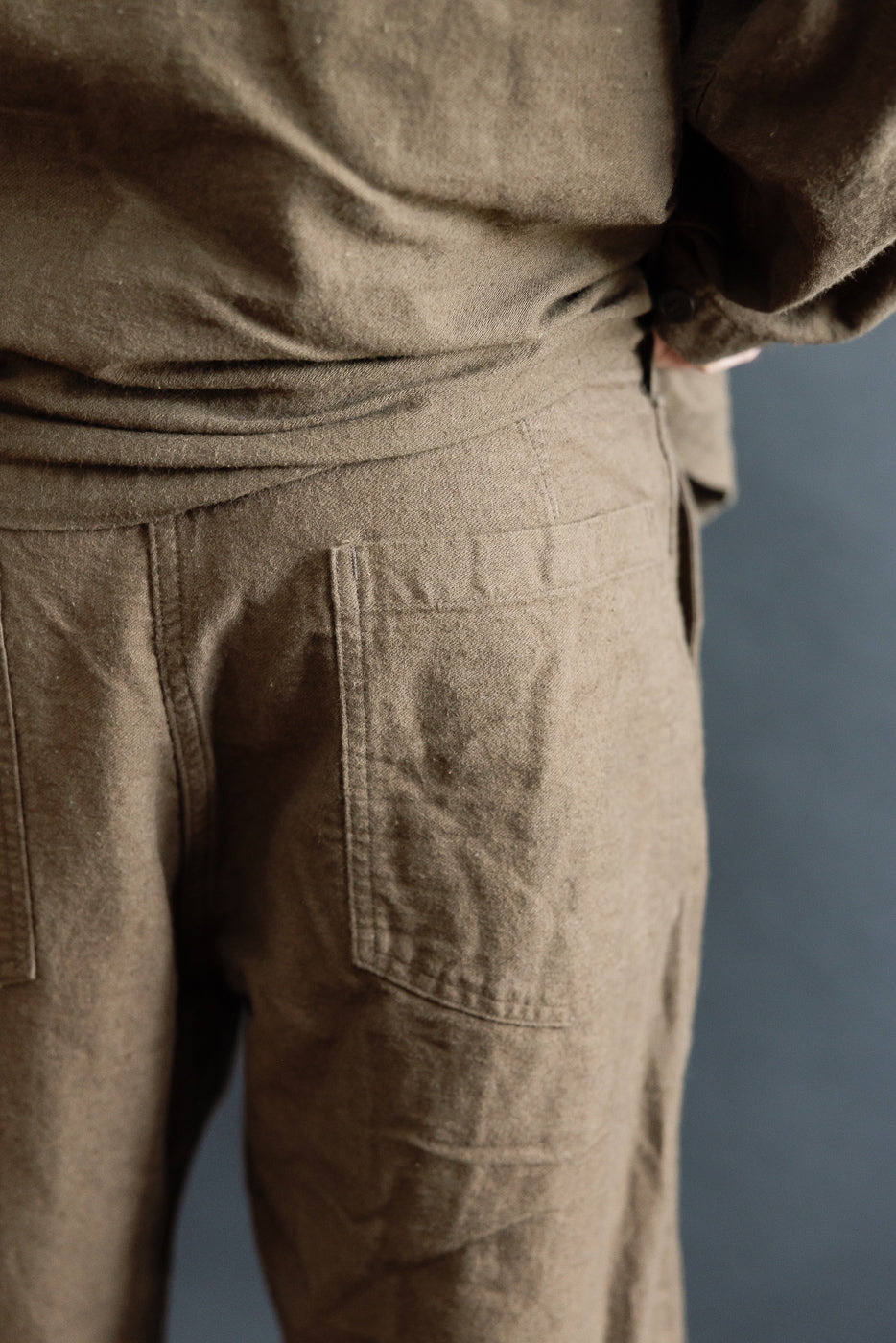 Close-up of back of coffee brown Orslow fatigue pants on male model, showing rear pockets and fabric texture.
