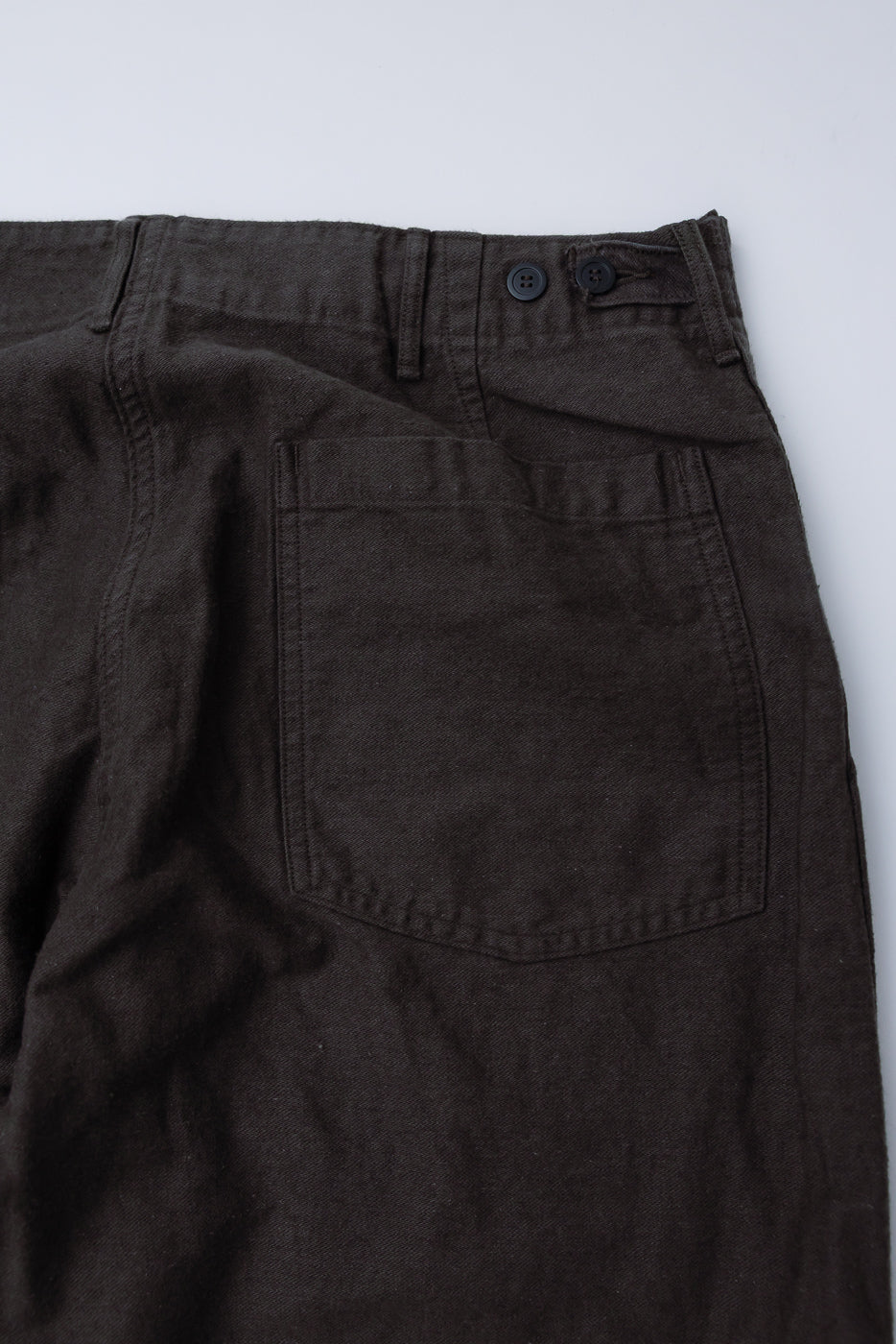 Close-up of orSlow fatigue pants back side, charcoal gray cotton linen, rear pocket and waist buttons visible