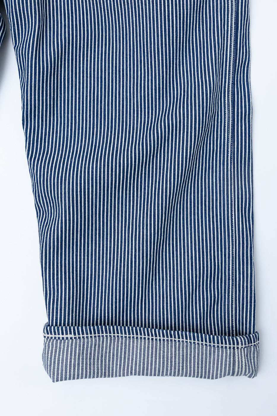 Close-up of indigo and ecru hickory striped painter pants leg with visible cuff and seam detail, front side.
