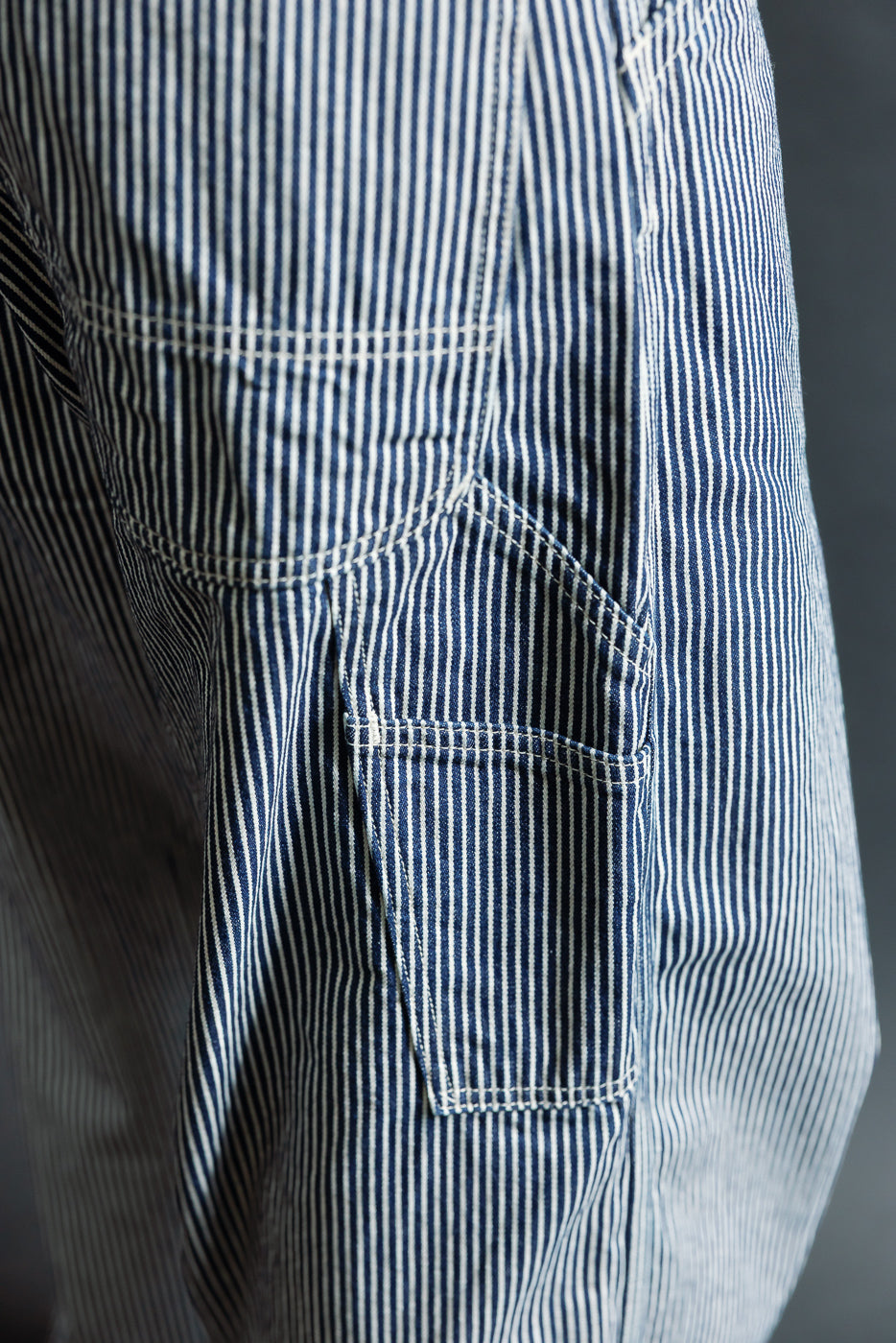 Close-up of side seam and pocket on hickory striped indigo painter pants, showing fabric texture and stitching details.