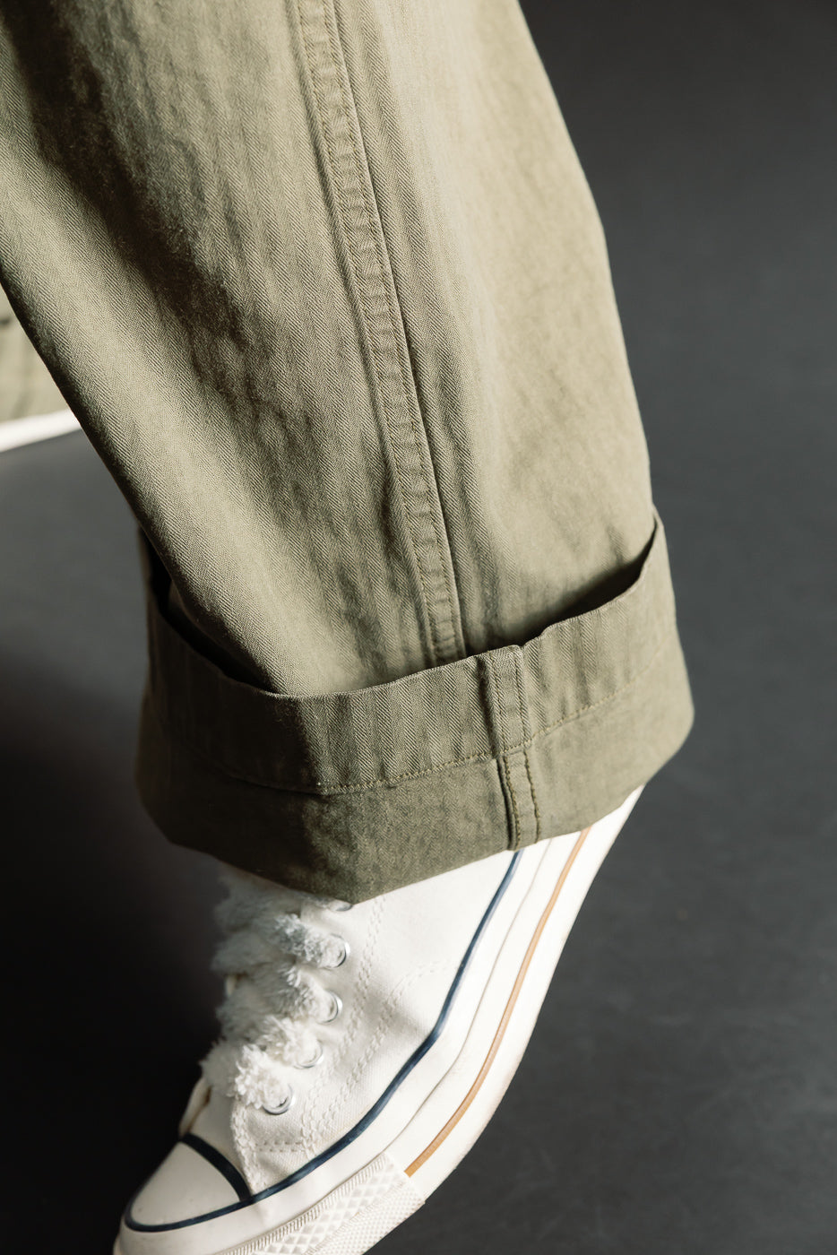 Close-up of hem and fabric texture on front lower leg of orSlow USMC herringbone utility trousers in dark olive, shown on male model.