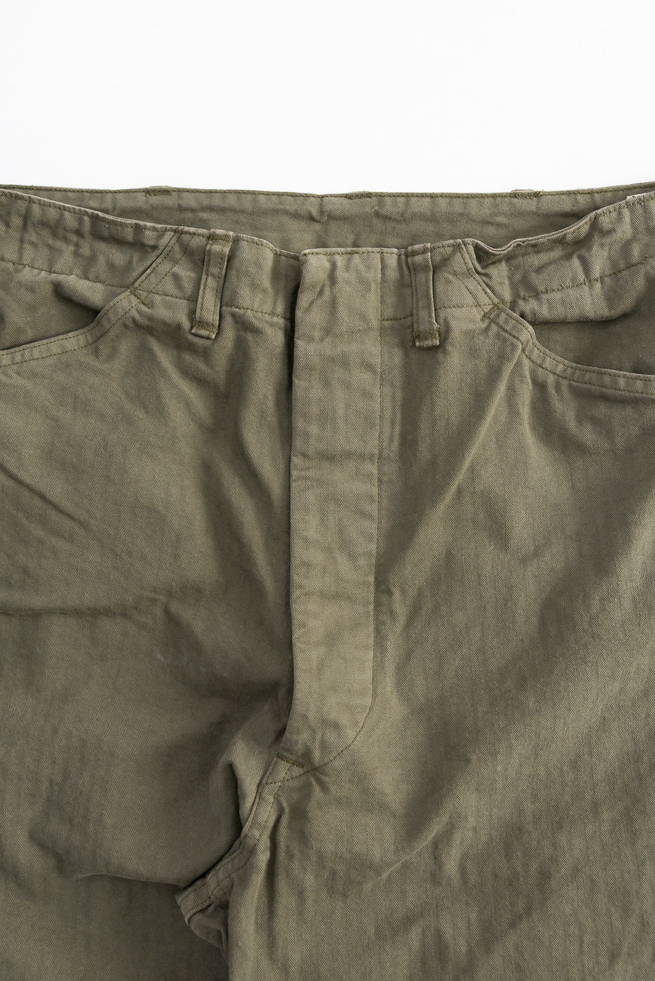 Close-up front view of orSlow USMC herringbone utility trousers in dark olive showing waistband, belt loops, and front pockets.