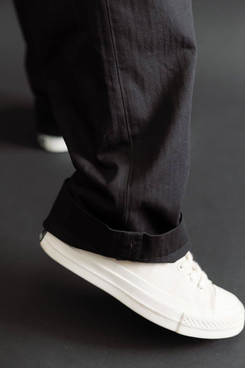 Close-up of the cuffed hem and ankle of black casual trousers worn with white sneakers.