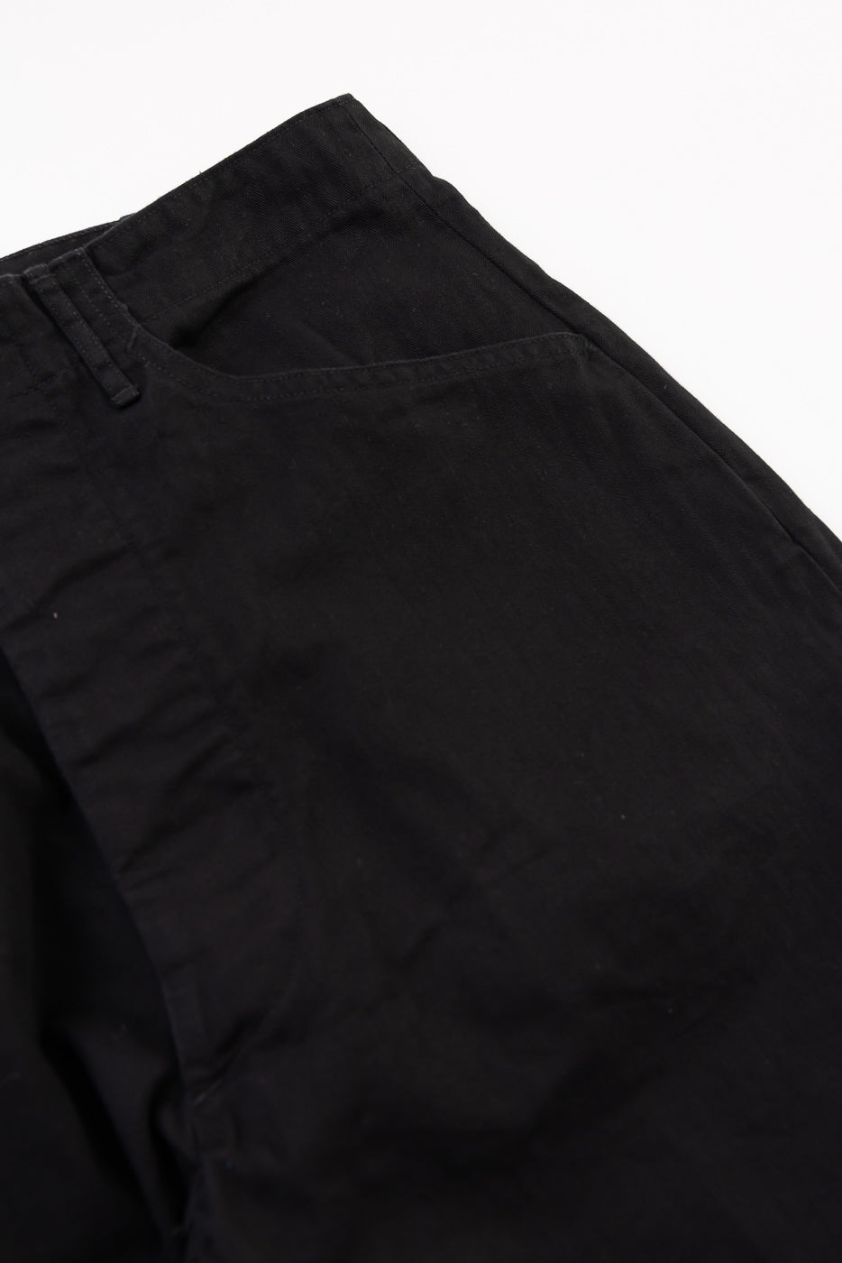Close-up of the front waistband and right hip pocket of black cotton trousers.