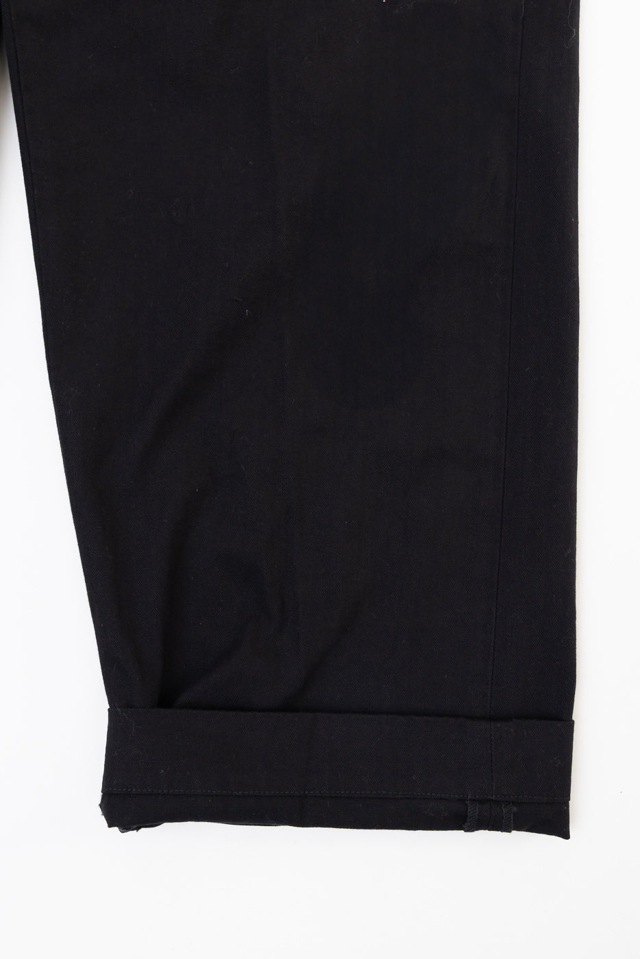 Close-up of the bottom hem and cuffed leg of black casual trousers, front view.