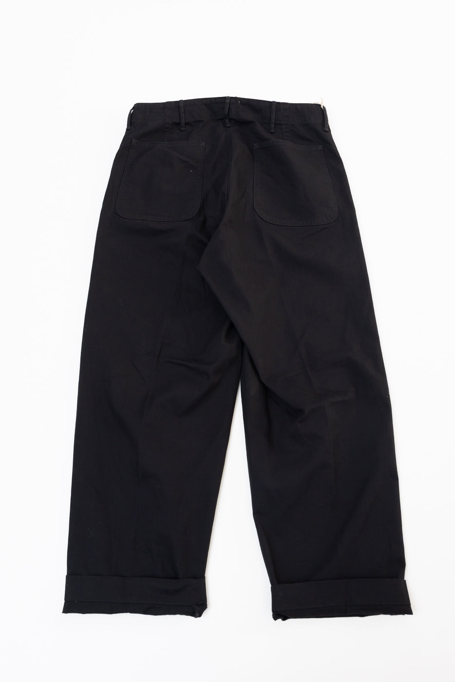 Back view flat lay of black wide-leg trousers showing rear patch pockets and cuffed hems.