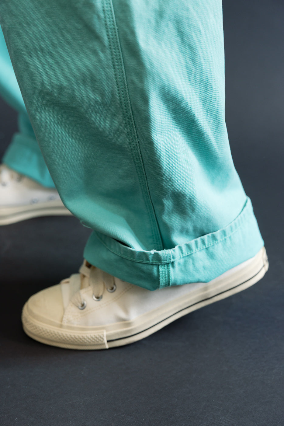 Close-up of the 01-5328-39SK Dad's Fit Painter's Pants Canvas - Turquoise, showcasing the cuffed teal-green pants and cream canvas sneakers, highlighting the pants' aged texture and brass UFO rivet detail.
