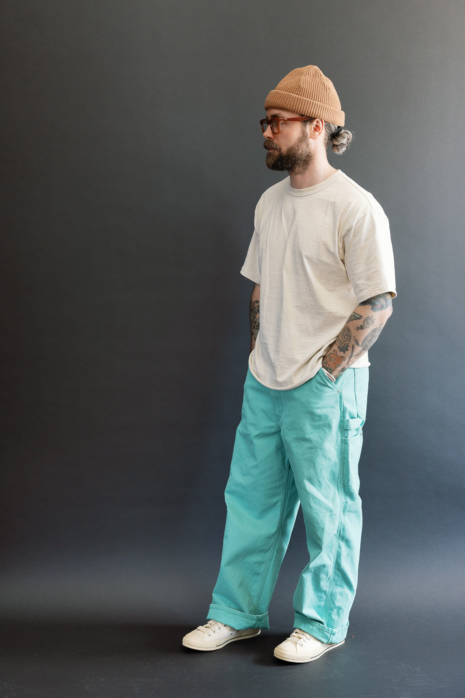 Model wearing 01-5328-39SK Dad's Fit Painter's Pants Canvas in Turquoise, showcasing the roomy fit with a light beige T-shirt, beanie, and white sneakers against a dark backdrop.