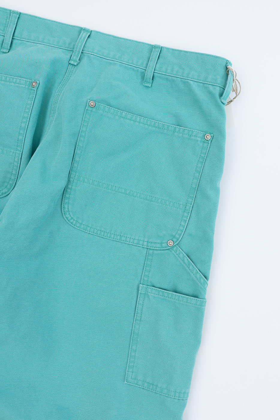 Close-up of 01-5328-39SK - Dad's Fit Painter's Pants Canvas - Turquoise, showcasing teal-green canvas trousers with reinforced patch pockets and brass rivets, emphasizing the aged, worn-in texture and sturdy design.