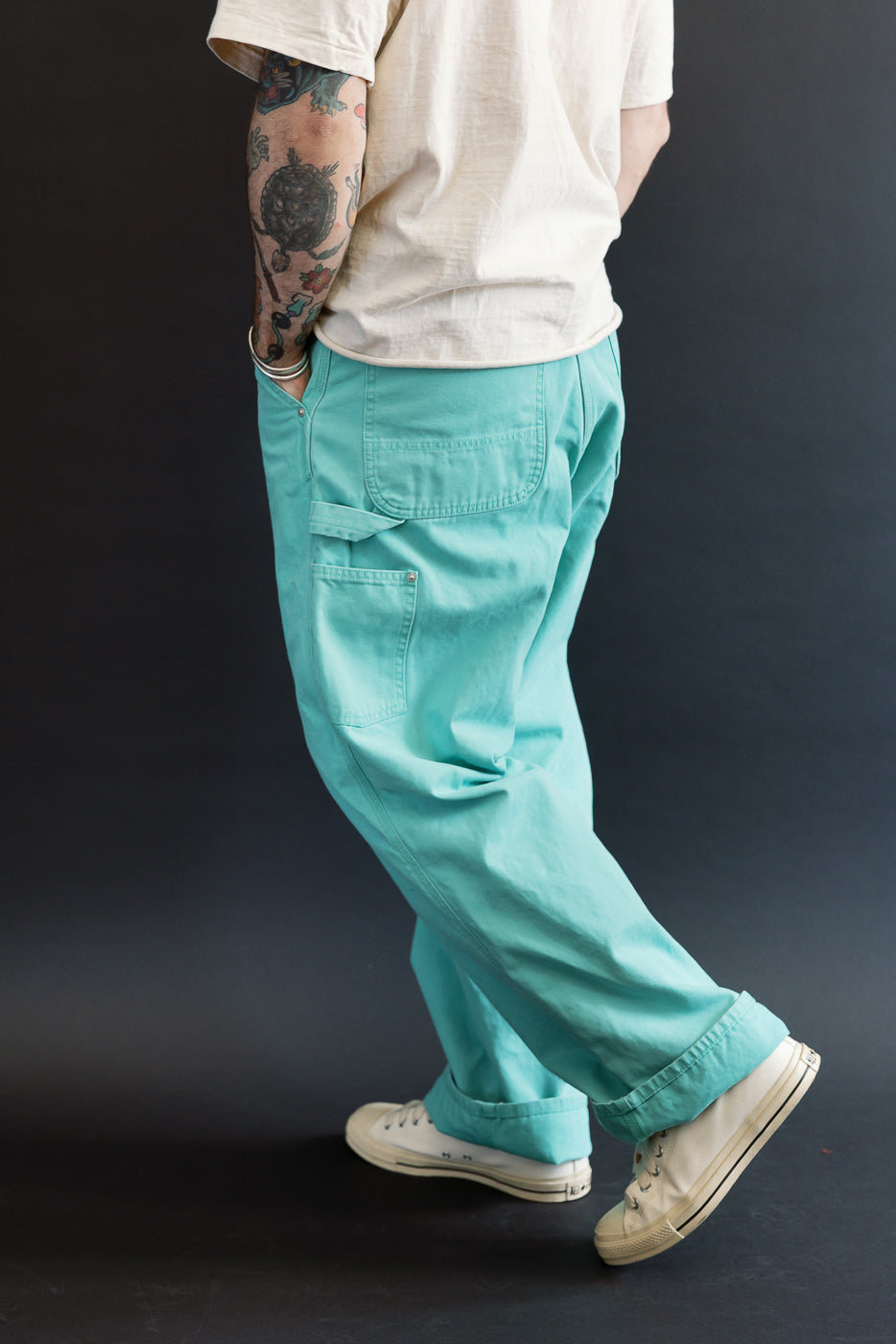 01-5328-39SK - Dad's Fit Painter's Pants Canvas - Turquoise showcased with utility pockets, worn-in duck cotton canvas, and brass rivet detailing, paired with white sneakers and a cream T-shirt.