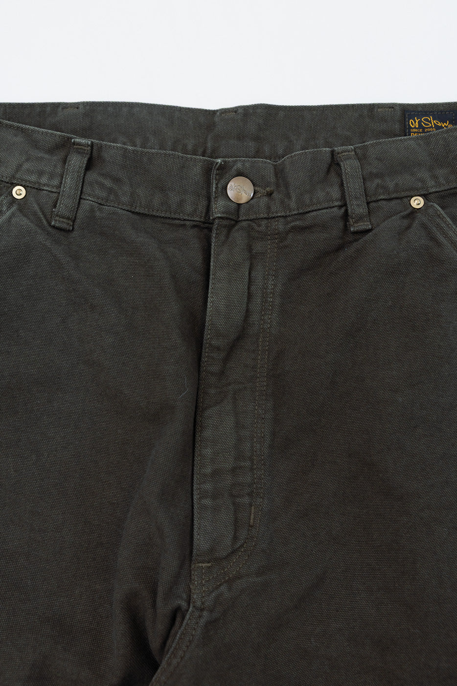 Close-up of the front waist and fly of dark grey trousers showing fabric texture and button.