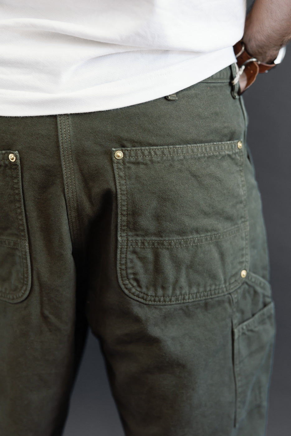 Close-up back view of a male model wearing olive green utility trousers showing the back pockets.