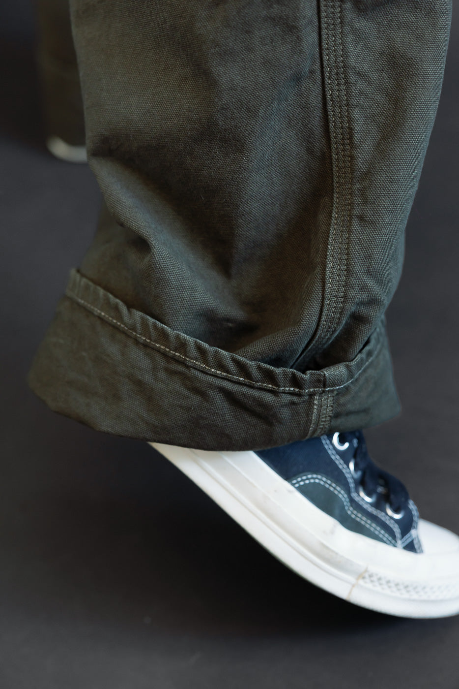 Close-up of the hem and cuff of olive green cotton trousers worn by a male model.