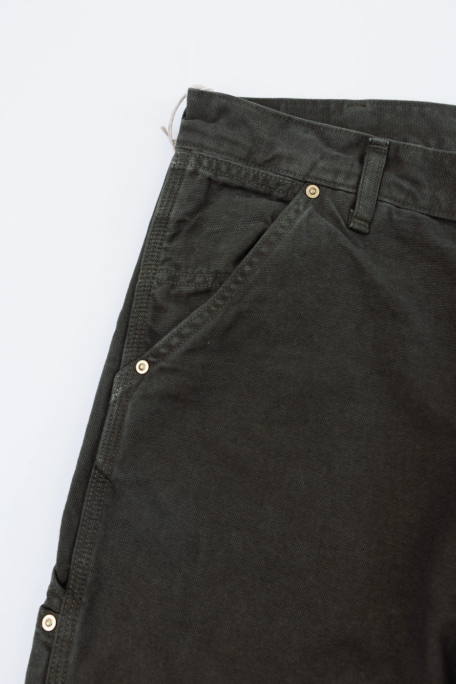 Close-up of the front left side of dark olive green canvas trousers showing pocket and belt loop.