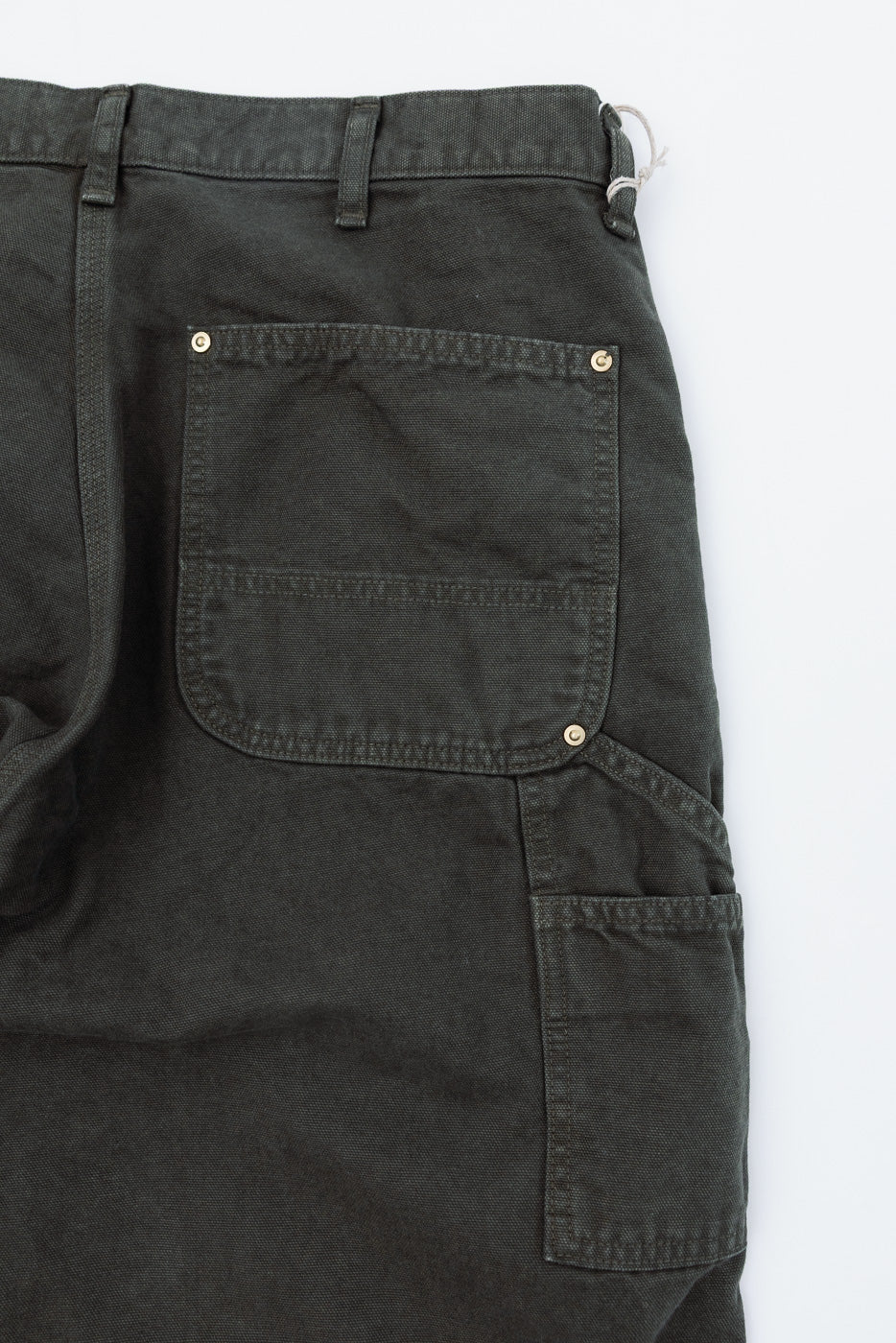 Close-up of the back of dark olive green work pants showing a large rear pocket and side utility pocket.