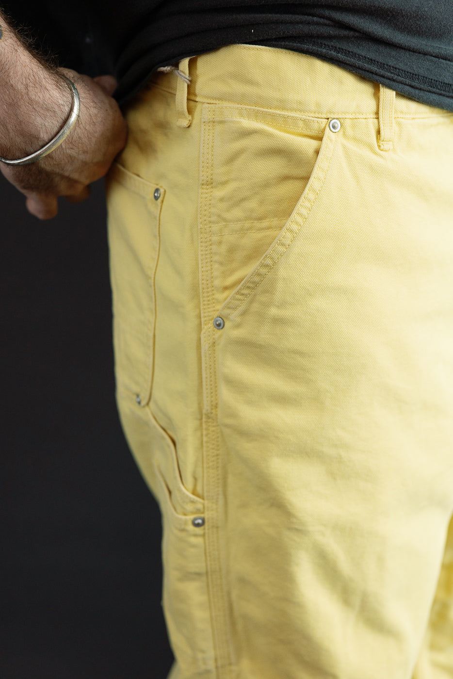 Close-up front view of male model’s yellow work pants, showing buttoned pockets, fabric texture, and side seam details.