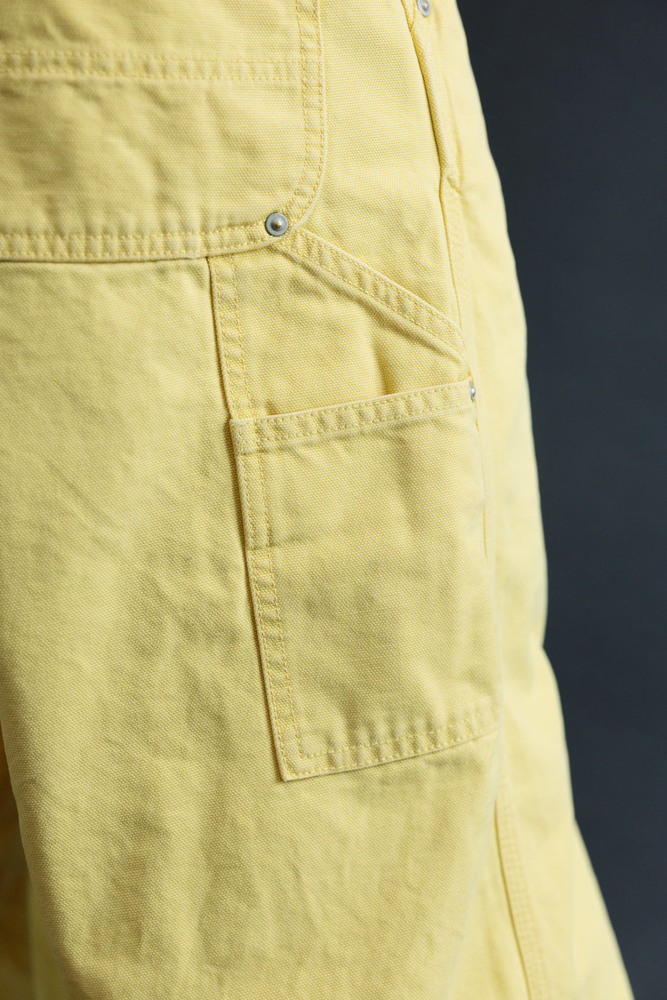 Close-up of male model's side, showing yellow cargo shorts with flap pocket, metal snap, and textured fabric
