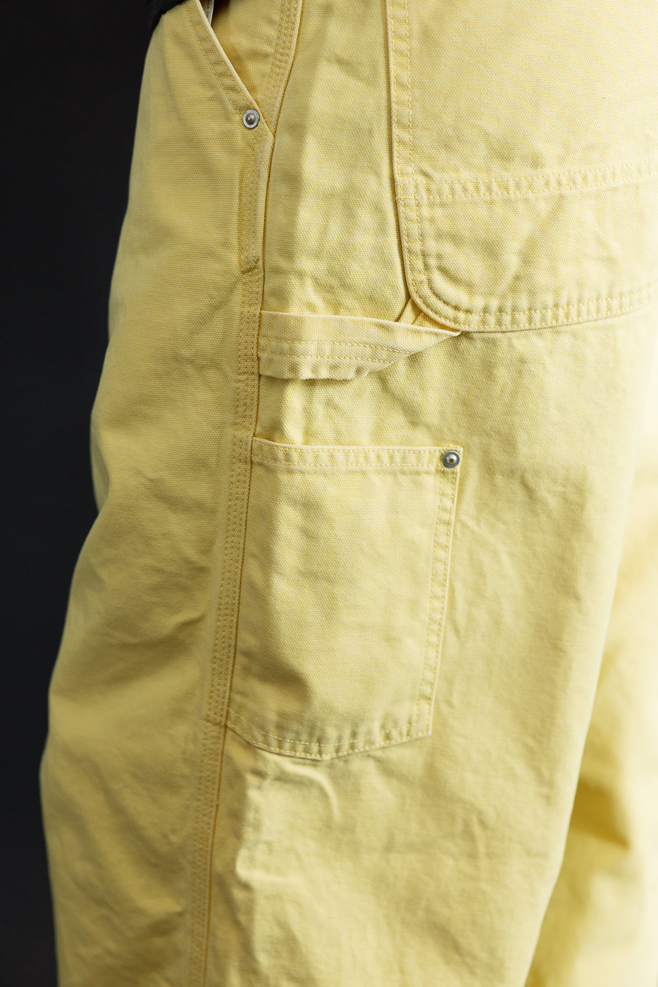 Close-up side view of yellow cargo shorts on male model, showing front pocket, button, and fabric texture