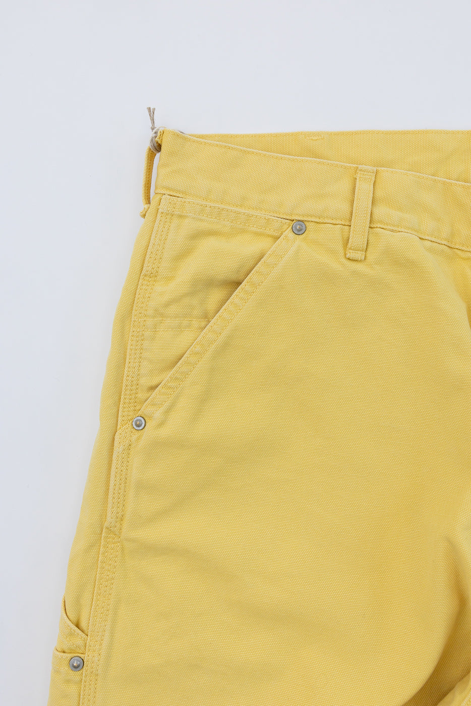 Close-up front view of yellow casual pants showing button fly, belt loops, and textured fabric detail