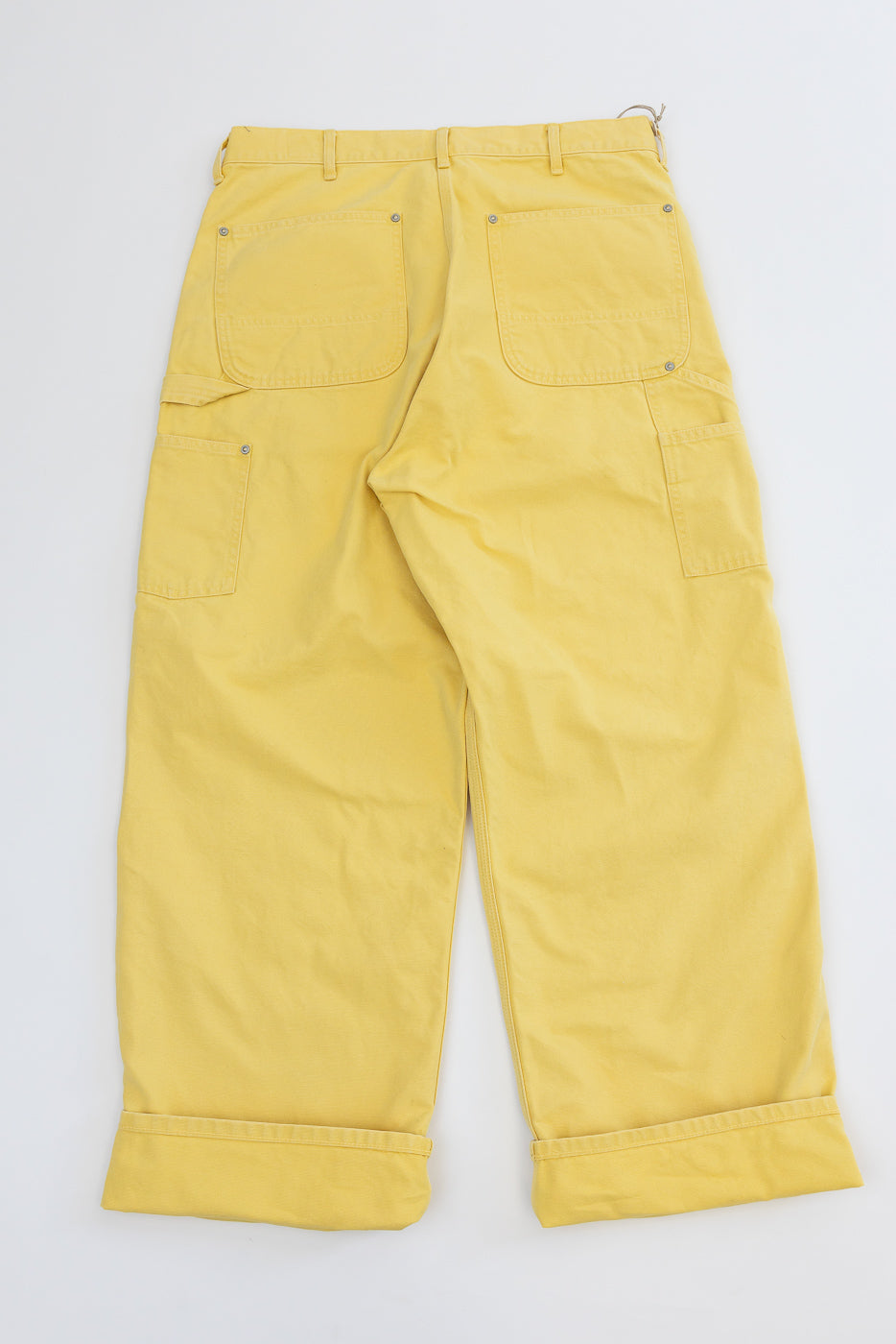 Flat lay back view of yellow cargo pants with flap pockets, cuffed hems, and metal rivets